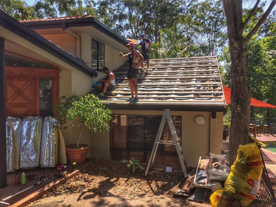 People Removing Tiles From a House Roof on a Sunny Day — Darren Smith Roofing In Glendale, NSW