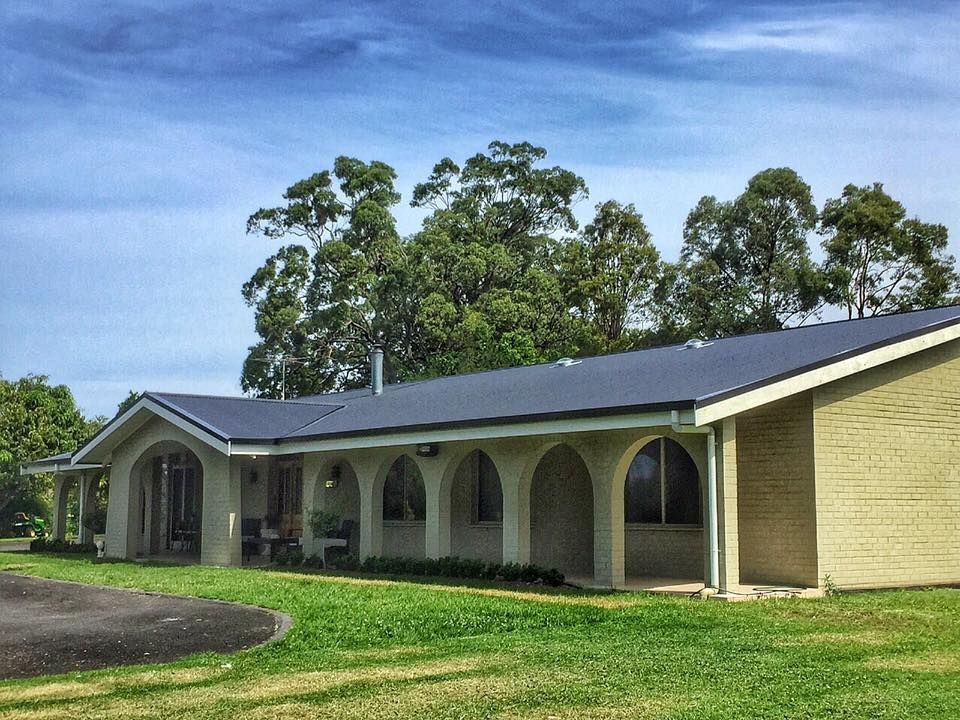 A Light-colored Building With Arched Windows on a Grassy Lawn — Darren Smith Roofing In Glendale, NSW
