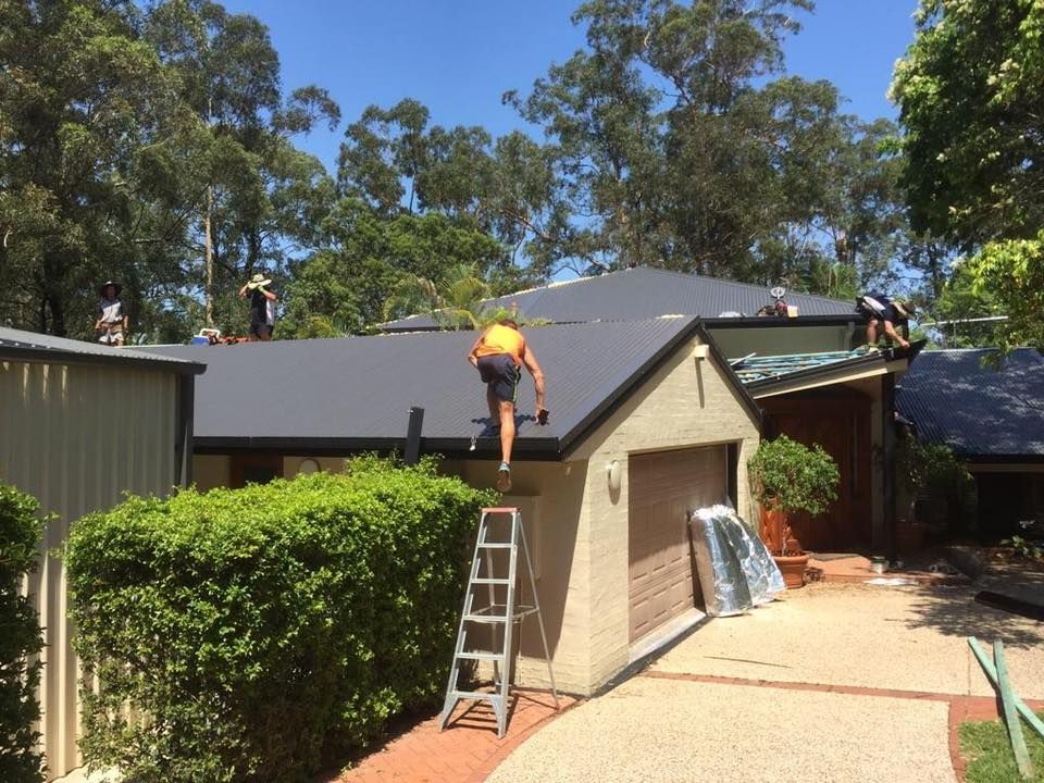 Roofers working on a residential house with a dark gray roof on a sunny day — Darren Smith Roofing In Glendale, NSW