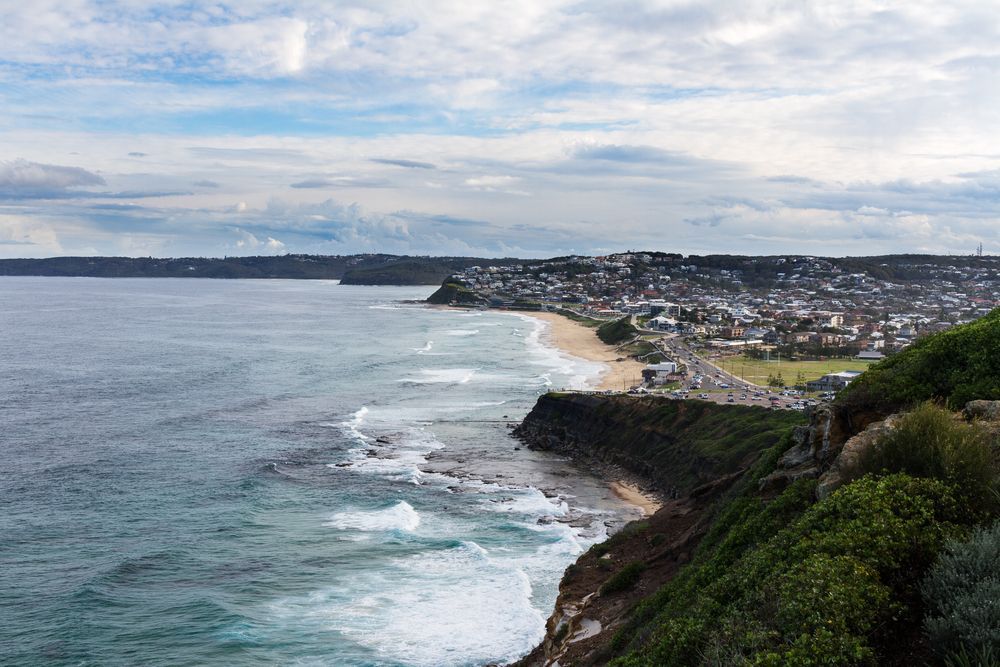 Coastal View With Ocean Waves, Beach, and Town Under a Cloudy Sky — Darren Smith Roofing In Merewether, NSW