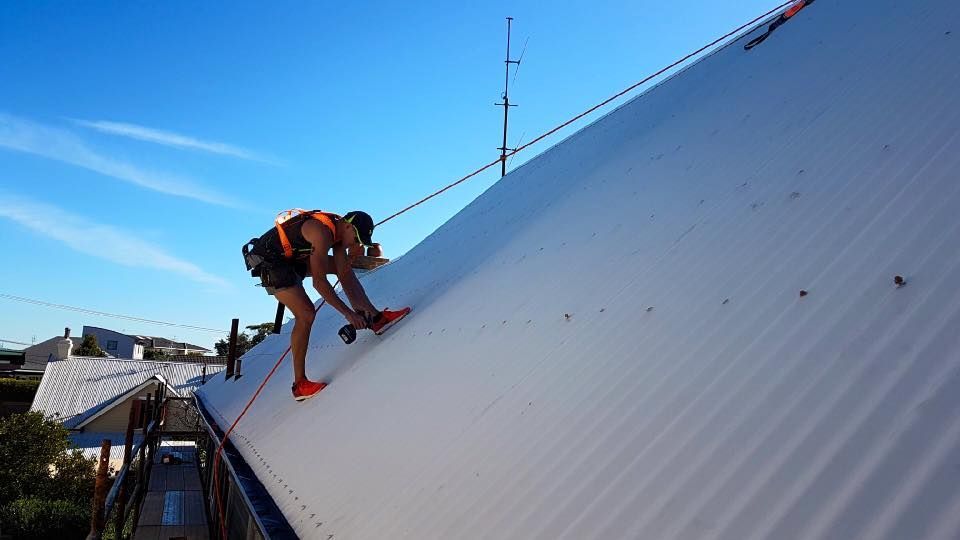 Person on a White Rooftop With Safety Harness Installing Something — Darren Smith Roofing In Glendale, NSW