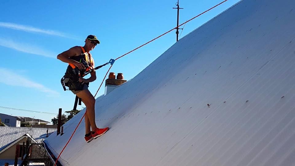 Man in Safety Harness Rappelling Down a White Rooftop on a Sunny Day — Darren Smith Roofing In Glendale, NSW