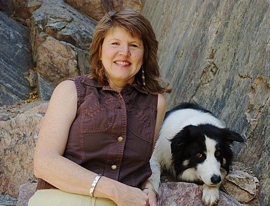 Woman in brown vest with black and white dog, against a rocky backdrop.
