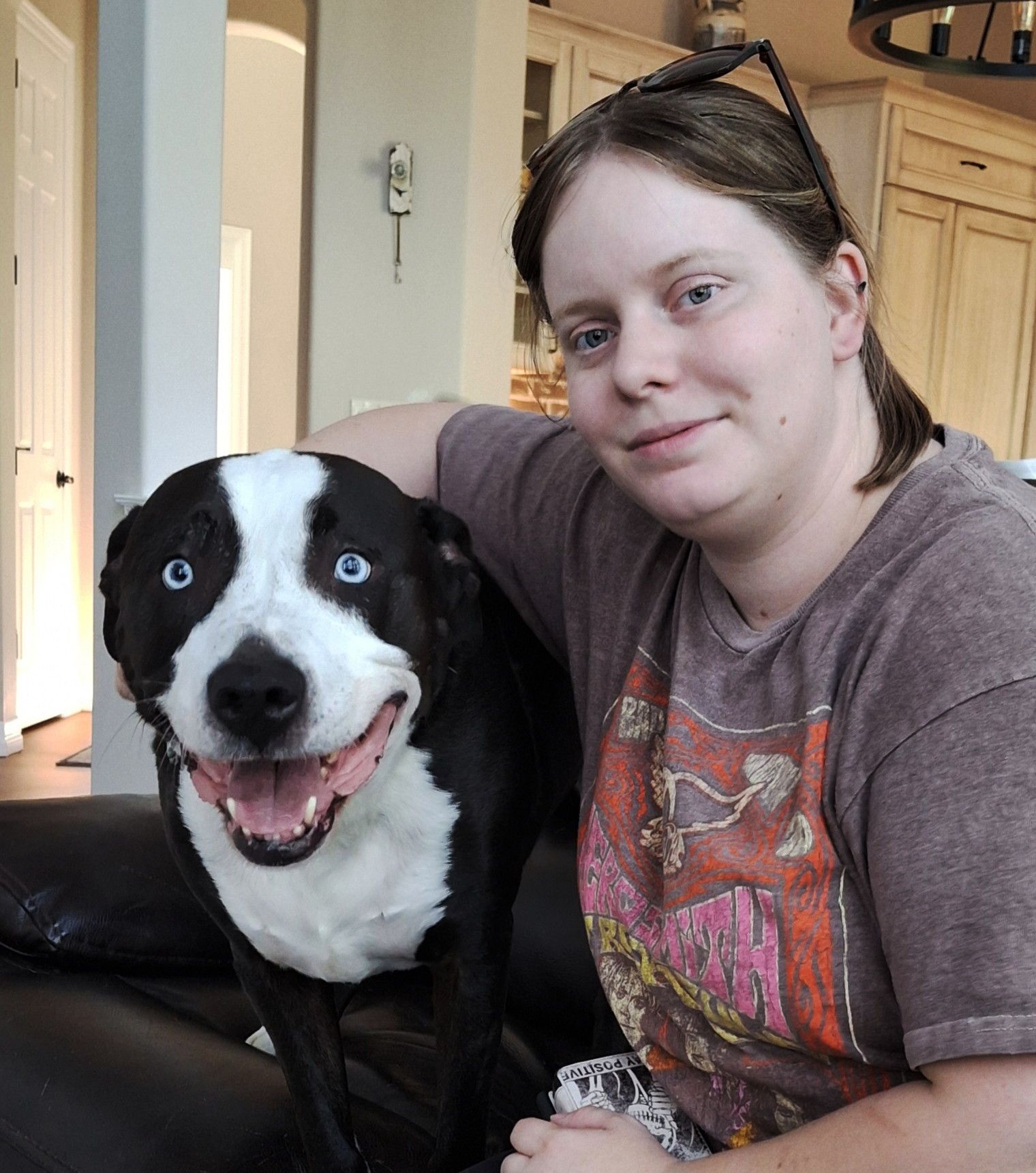 Woman with brown hair and eyeglasses smiles next to a black and white dog with blue eyes.