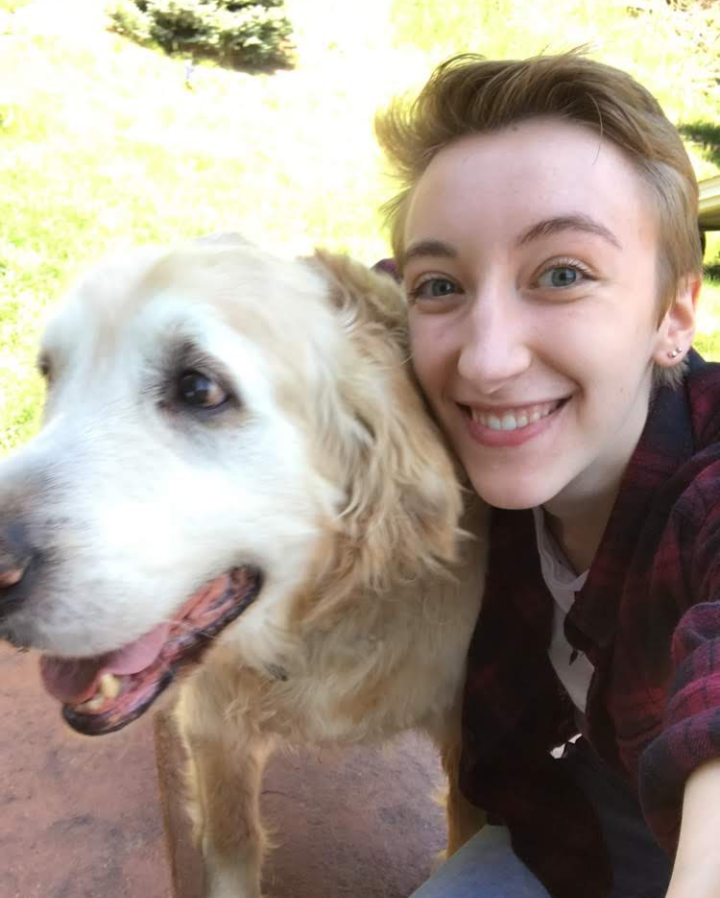 Woman with short hair smiles next to a golden retriever outside.