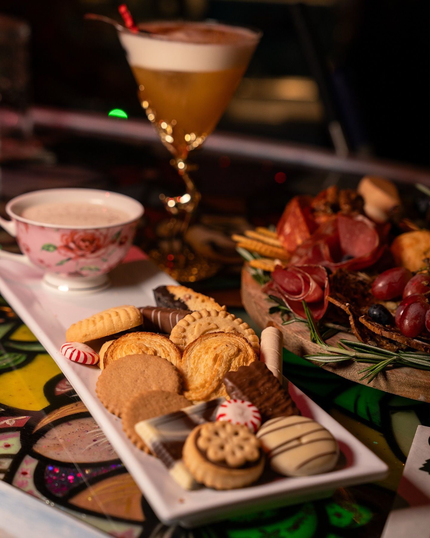 Cocktail, cookies, teacup, and charcuterie board on a table. Dark setting with colorful accents.https://www.hight-orlando.com/