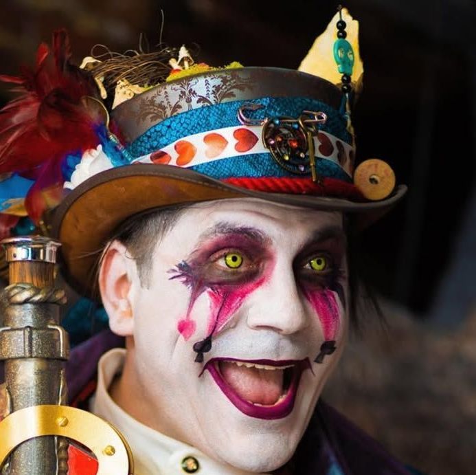Man with clown makeup and steampunk hat smiles widely.