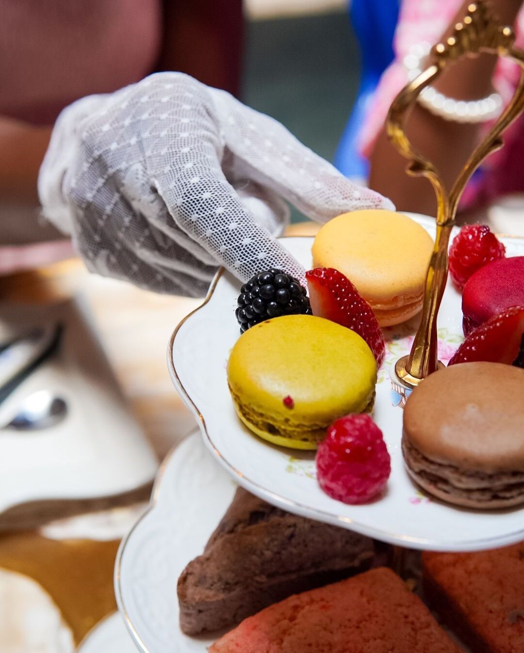 Hand in white lace glove holding a tiered tray of macarons and berries at a tea party.https://www.hight-orlando.com/