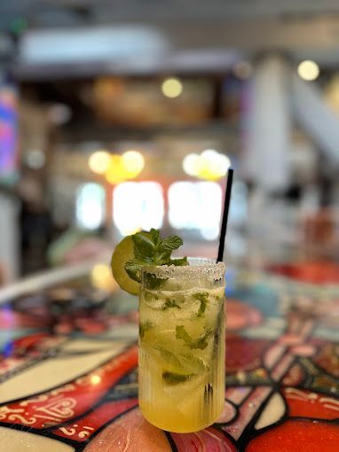Mojito cocktail in a glass with lime, mint, and a sugar rim, on a colorful bar.