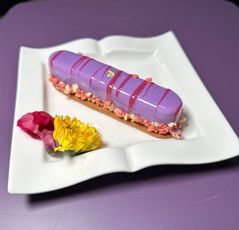 A purple glazed eclair on a white plate, decorated with pink accents, yellow and red flowers.DownTown Orlando 