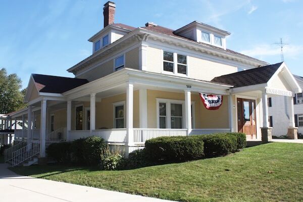 The front door of a house with a porch and plants in front of it.