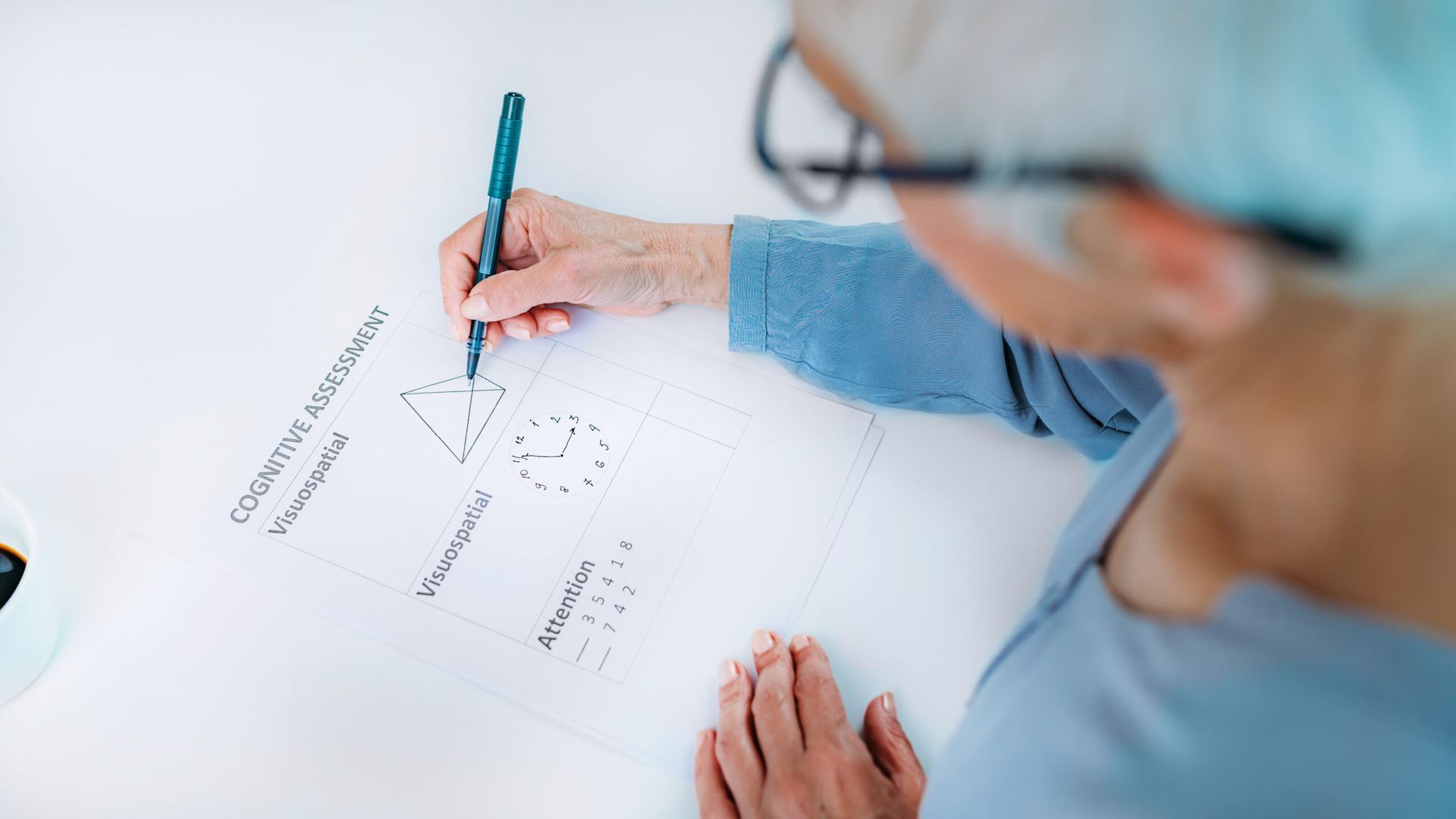 Person wearing glasses writing on a paper with shapes and math problems.
