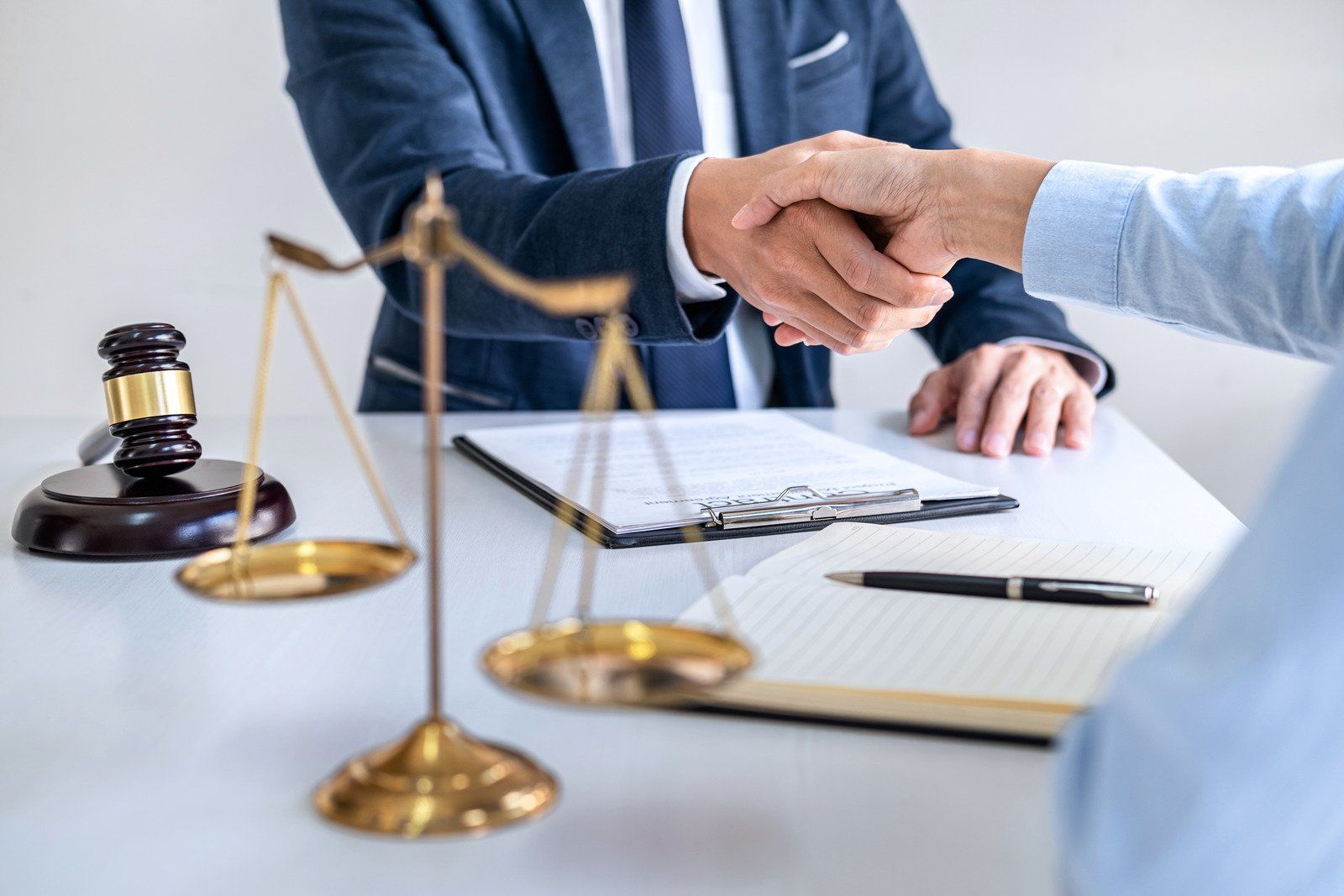Lawyer and client shaking hands over a desk with scales of justice and documents.