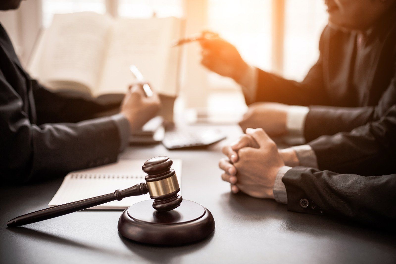 Gavel on a table with lawyers, book, and laptop; meeting in a room.