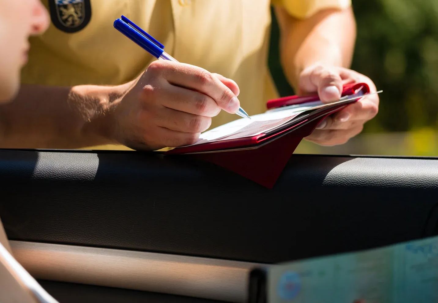 Police officer writing a citation for a driver at a car window.