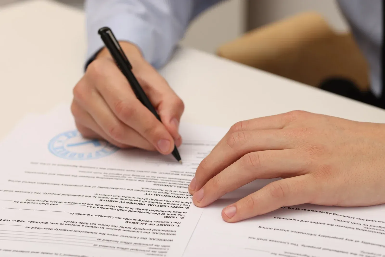 Person's hands writing with a pen on paper, close up. A document is on a desk.