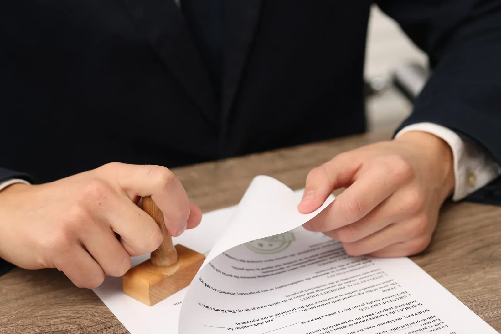 Person stamping a document with a wooden stamp; close-up of hands and paper on a desk.