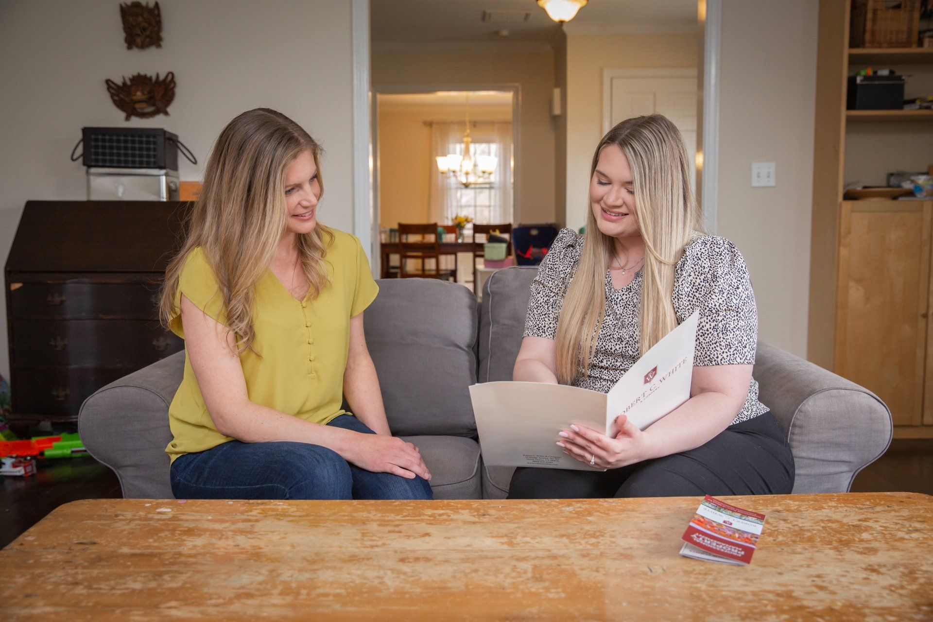 Two women are sitting on a couch looking at a piece of paper.