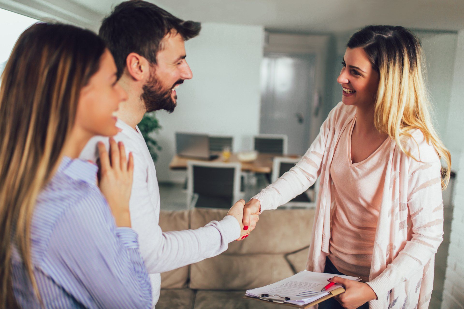 A woman is shaking hands with a man and a woman in a living room.