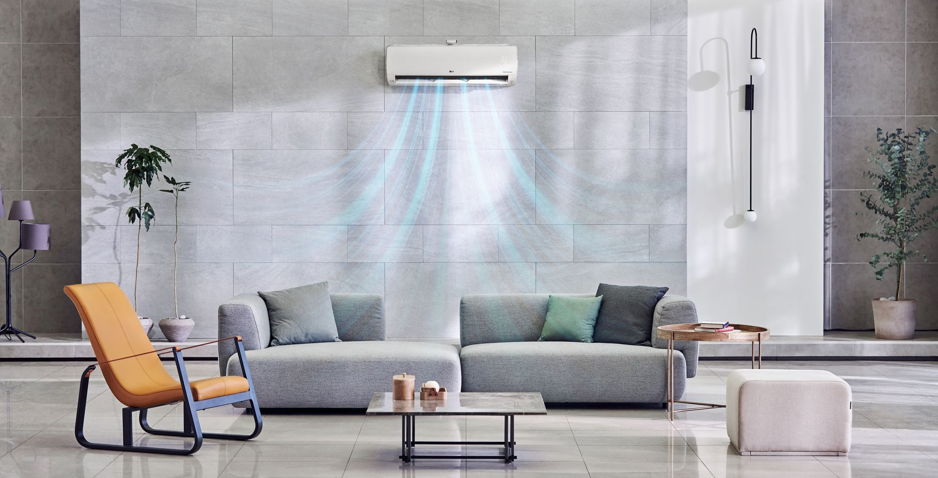 Ein Klimagerät hängt an einer grauen Plattenwand über einem Sofa