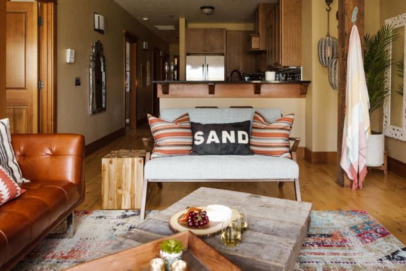 A living room with a couch , coffee table , and a pillow that says sand.
