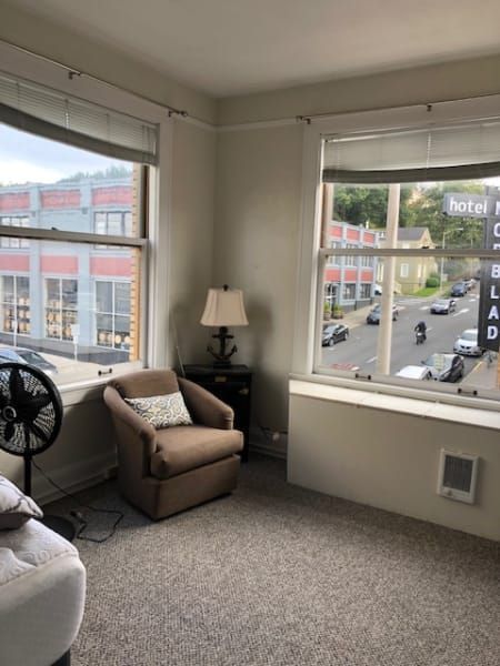 A living room with a chair , lamp , fan and a large window.
