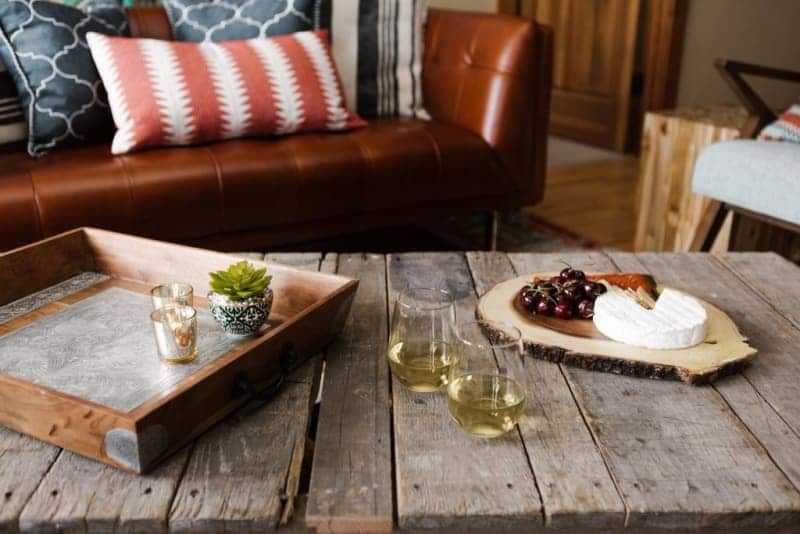 A wooden table with a tray of food and wine glasses on it in a living room.