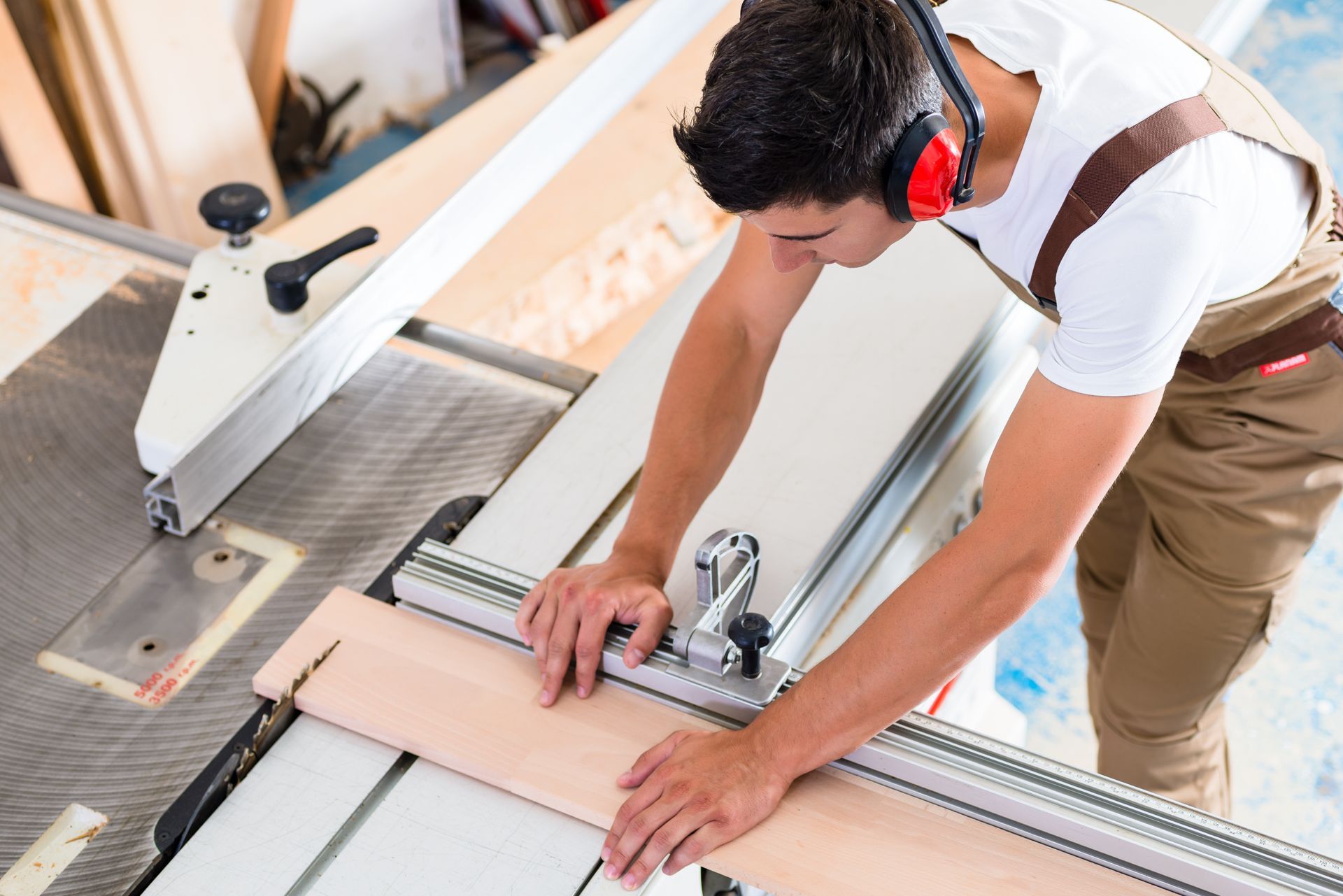 Bright white kitchen featuring custom cabinets with gold hardware and a large center island. Person measuring a wood board on a miter saw table in a workshop.