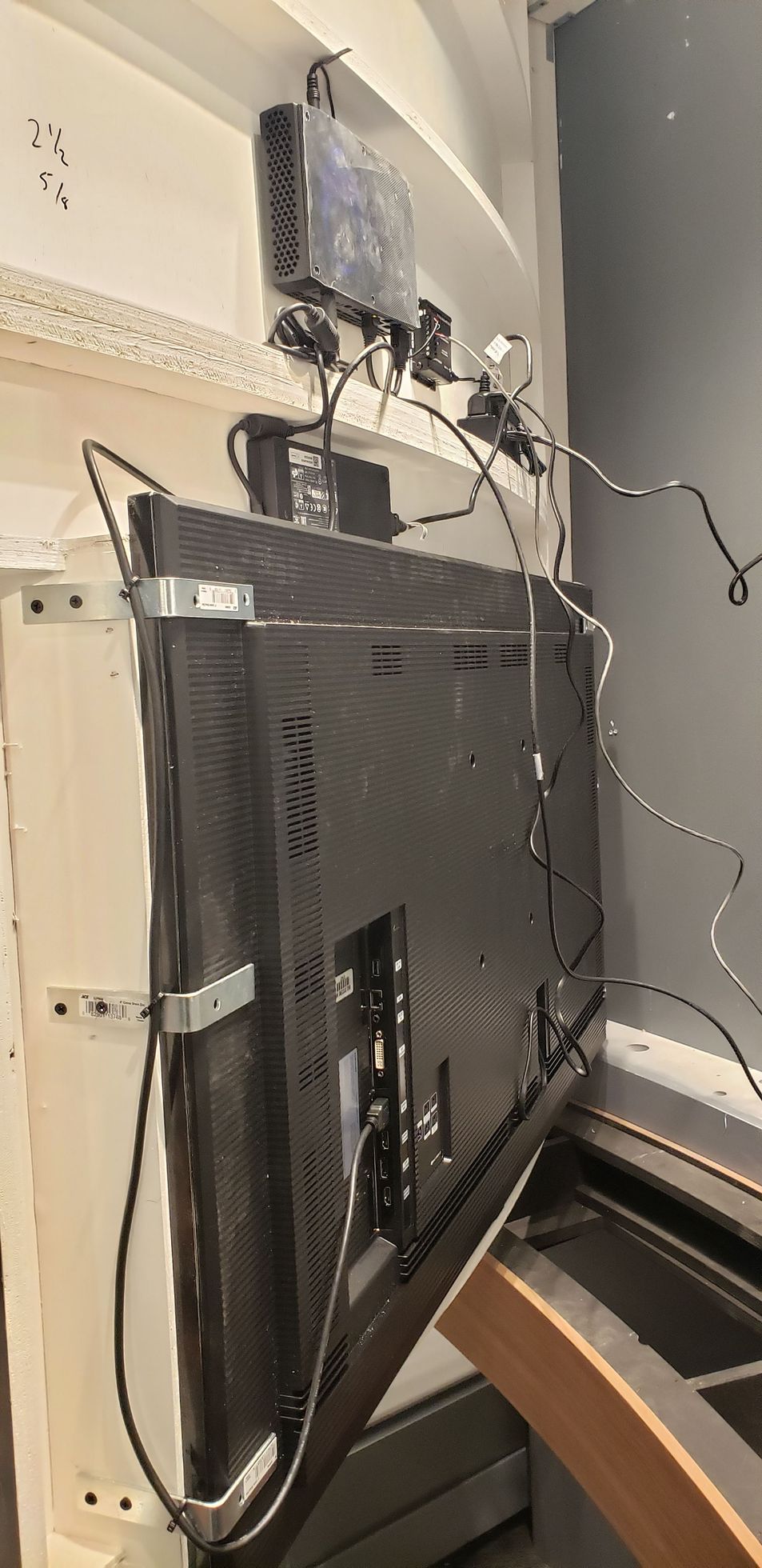 A television is hanging on a wall with a lot of wires coming out of it.