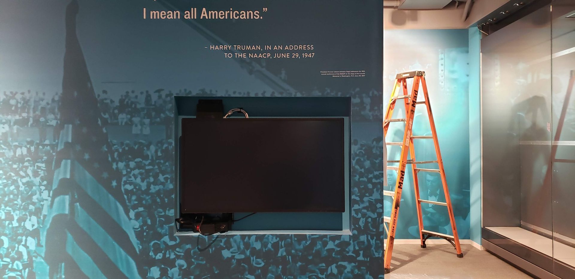 A ladder is sitting in front of a wall with a tv on it