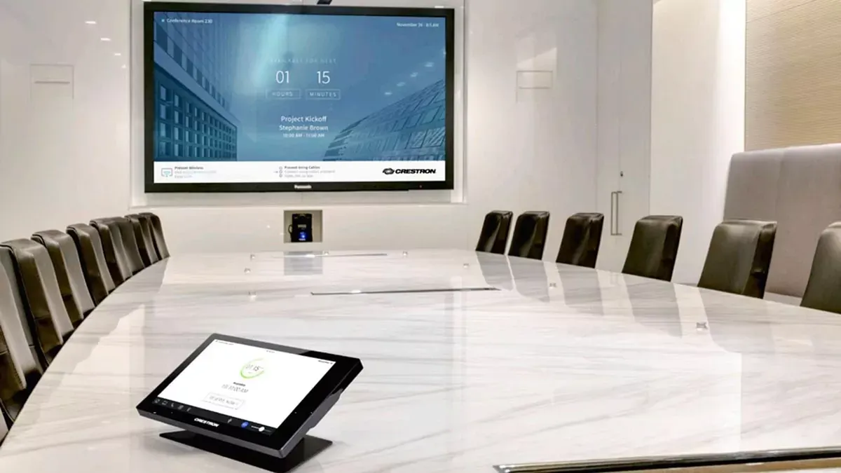 A conference room with a large screen on the wall and a tablet on the table.