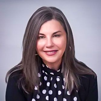 A woman with purple hair and a black jacket is smiling for the camera.