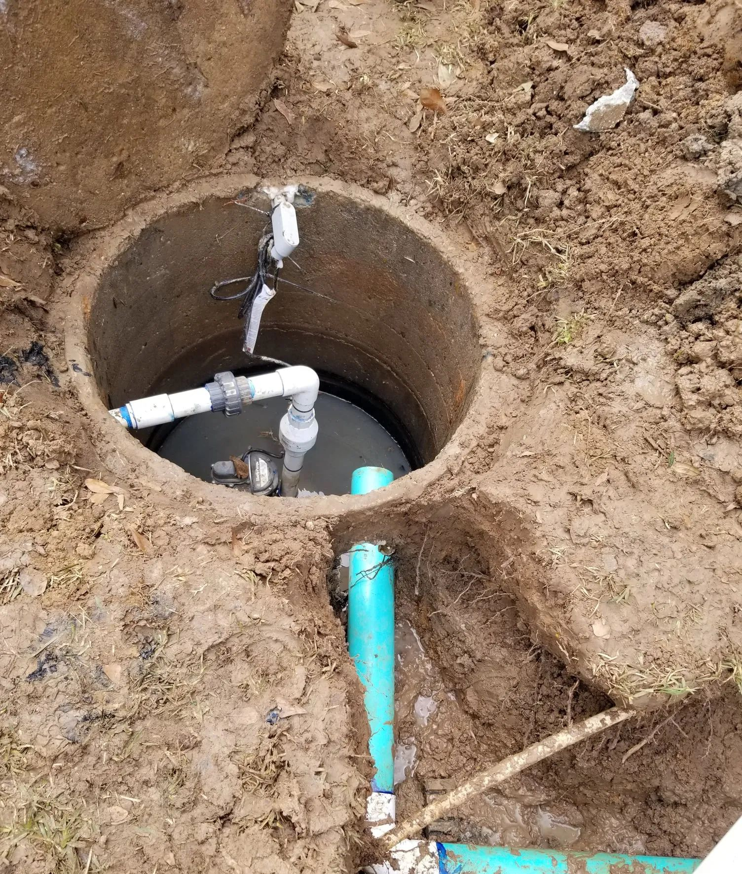 Open ground utility pit with PVC pipes and a blue pipe emerging from the soil.