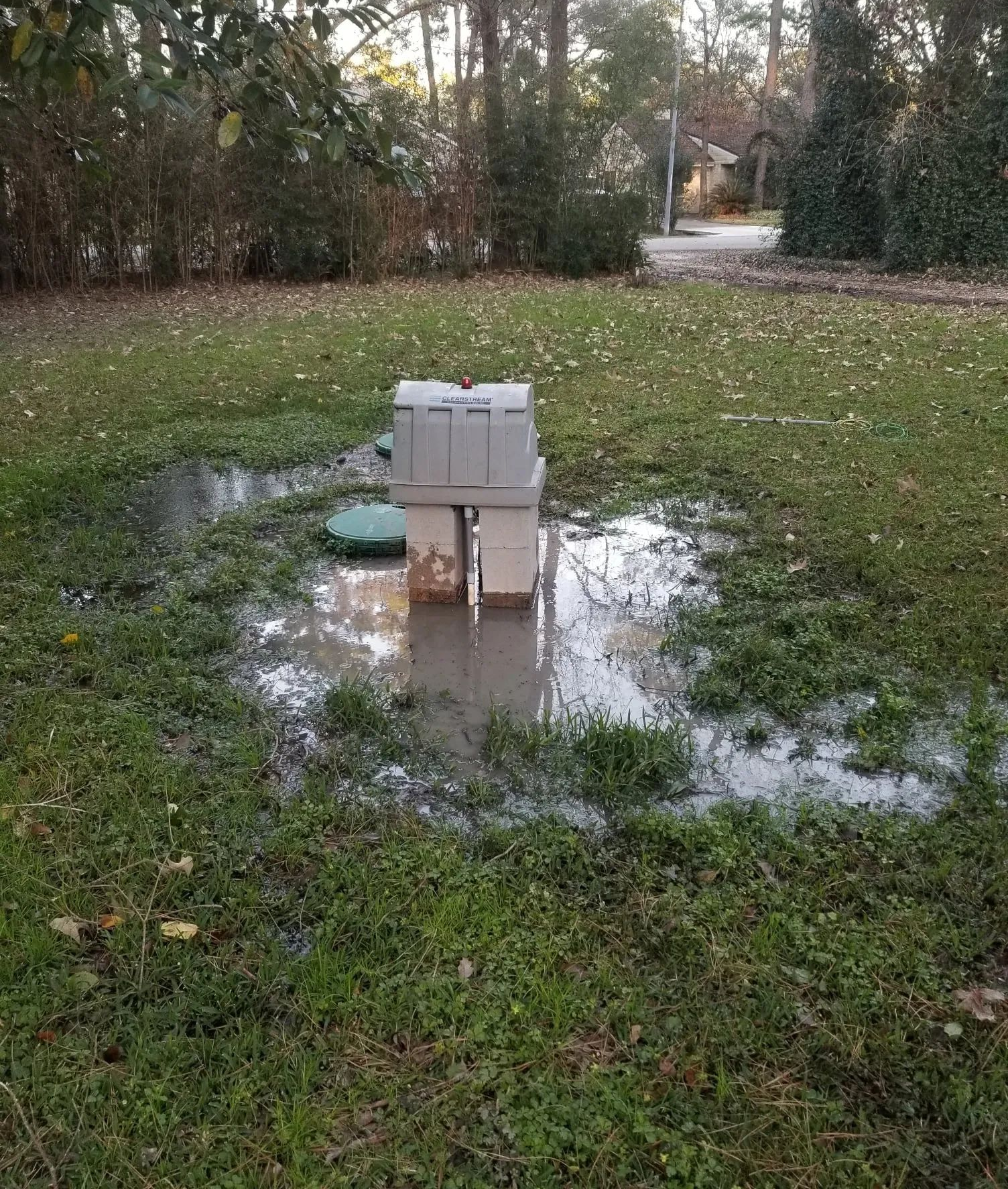 White chair in a muddy puddle on a grassy yard with trees in the background