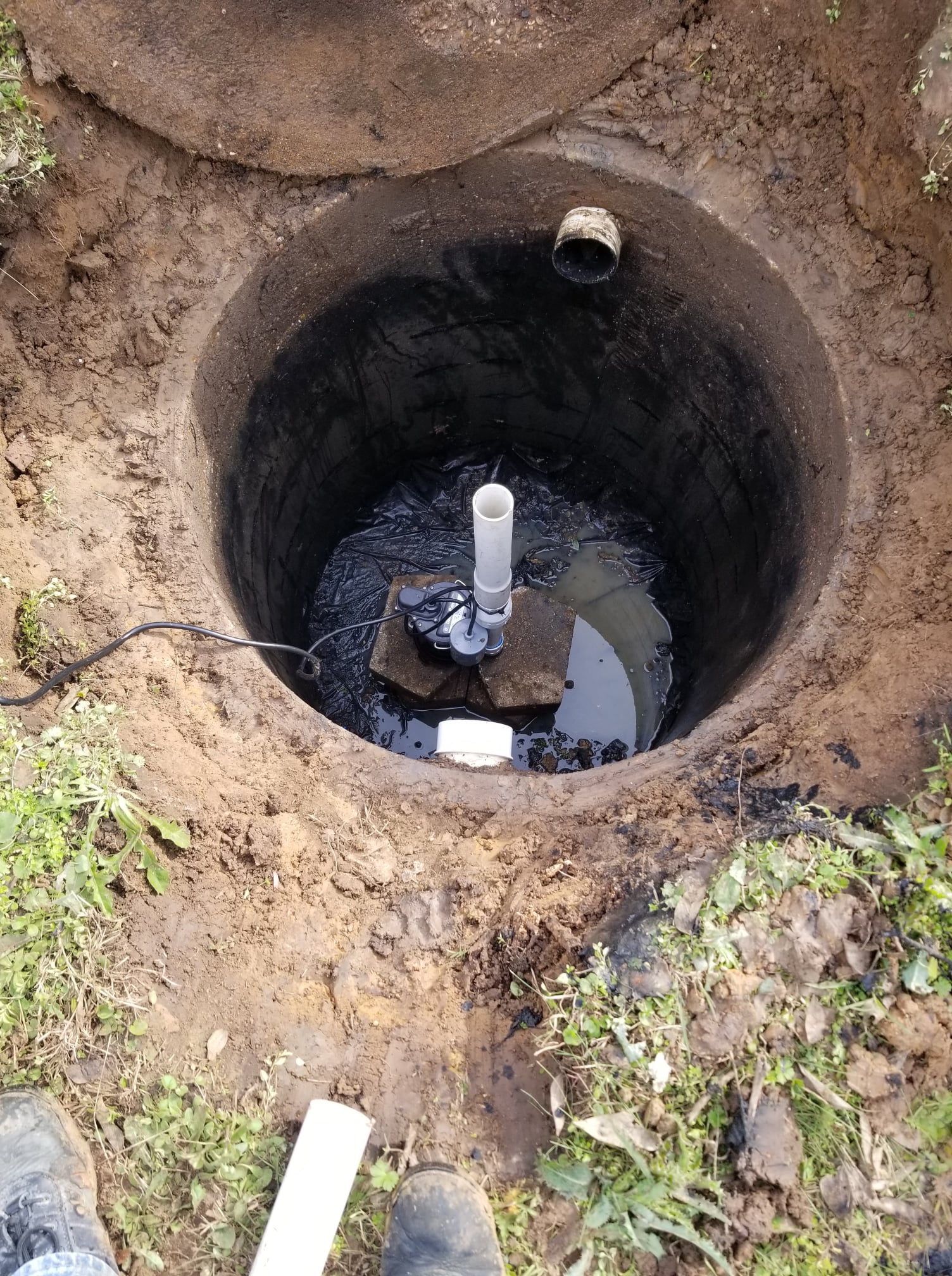 Open septic tank with water and pipes in a dirt hole.