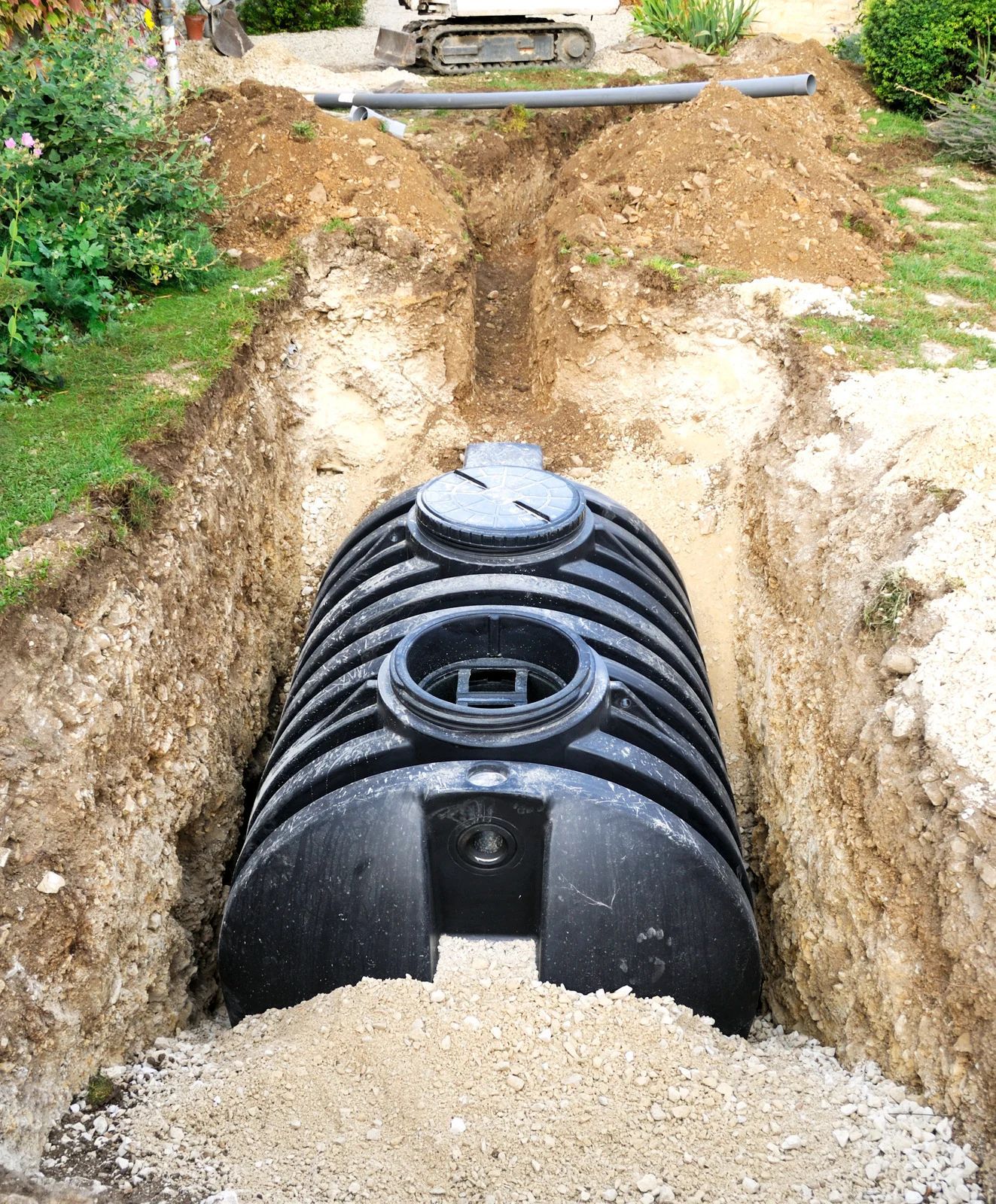 Black underground tank installed in a trench, surrounded by dirt and gravel on a construction site