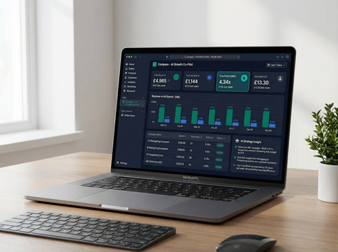 A laptop on a wooden desk displays a business analytics dashboard with charts and data, next to a keyboard and plant.