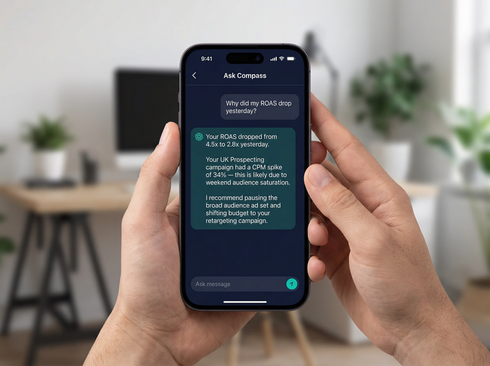 Hands hold a smartphone displaying a chat message on a dark-themed screen in a blurred office setting.