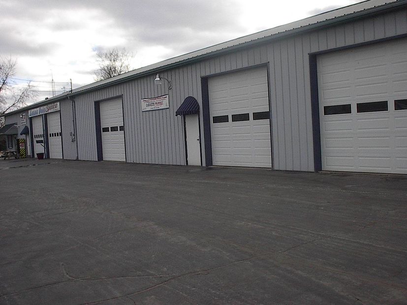 Row of gray industrial garage units with closed white doors along an empty paved lot