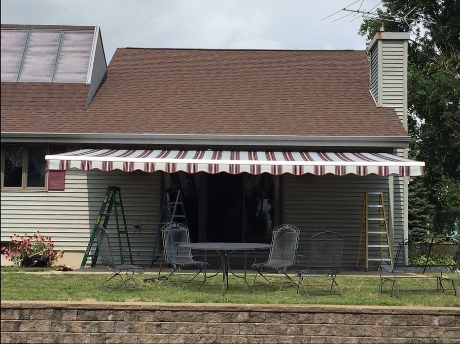 House with striped awning over a patio, with ladders and outdoor furniture in front