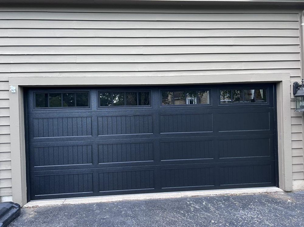Gray two-car garage with black doors and small windows beneath beige siding
