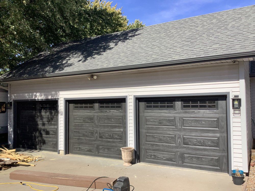 Three-car garage with gray doors and dark shingled roof in daylight
