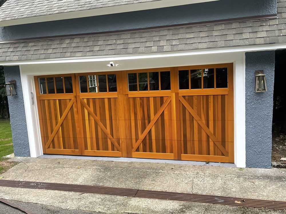 Wooden garage doors on a gray house with white trim and a shingled roof