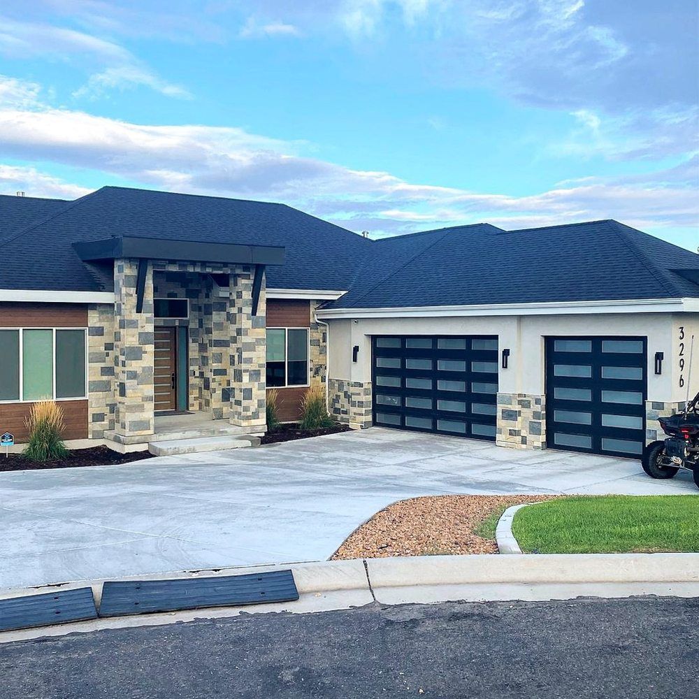 Modern single-story house with stone entry, dark roof, and three-car garage on a curved driveway