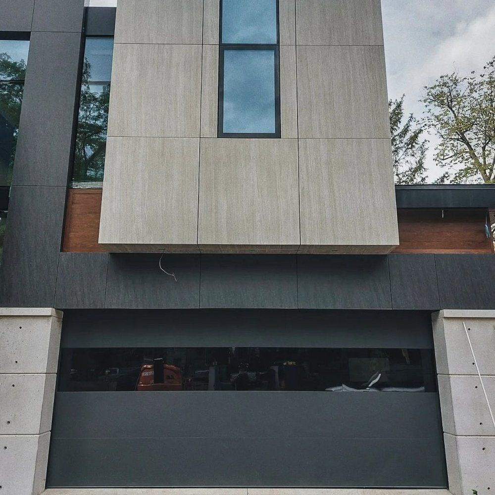 Modern gray-and-black building facade with large dark windows and a central vertical window panel