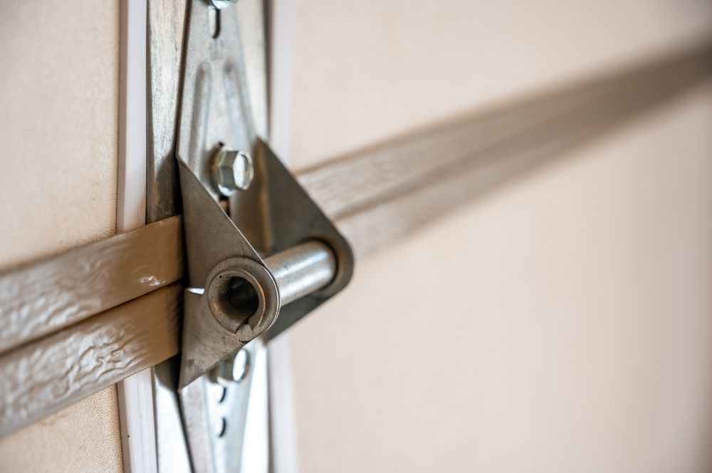 Close-up of a garage door hinge and roller bracket in beige and silver metal.
