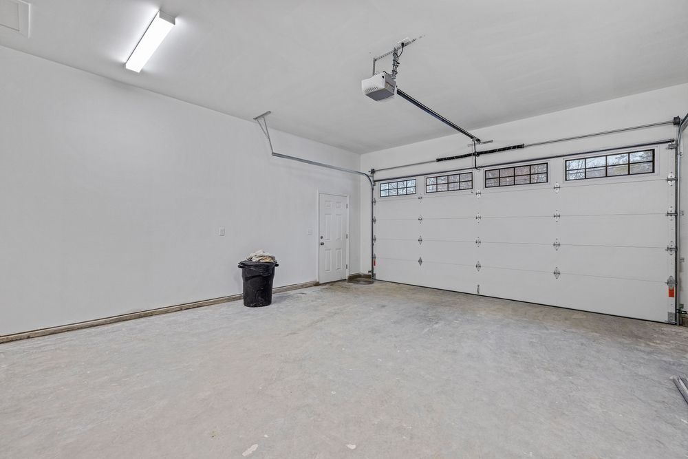 Empty white garage with a closed overhead door and a trash can near the wall