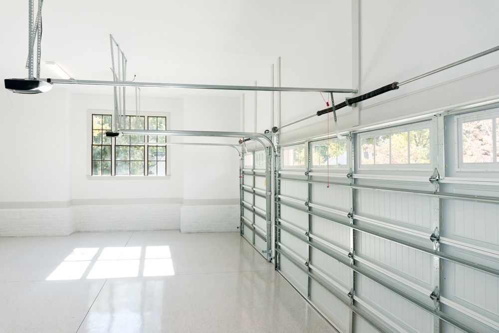 Empty white garage interior with windows, overhead tracks, and a sectional garage door on the right