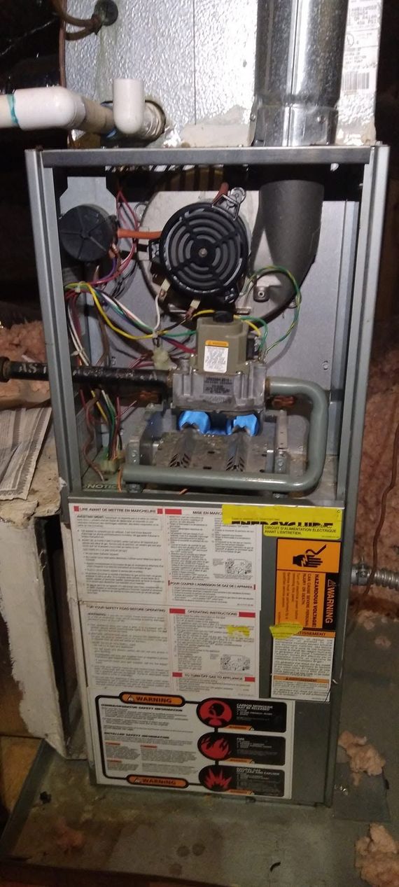 Open furnace with exposed wiring, fan, and service label in a utility closet
