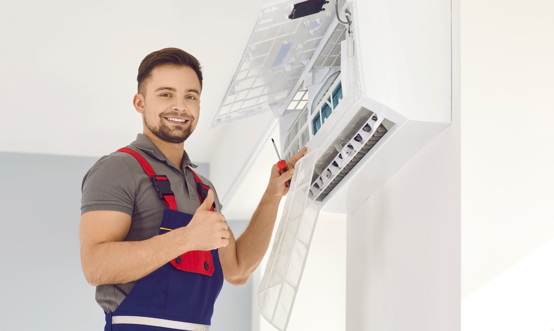 Technician in red overalls adjusting an indoor air conditioner unit on a wall